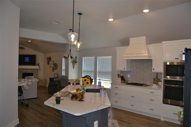 kitchen featuring premium range hood, stainless steel appliances, vaulted ceiling, a center island with sink, and white cabinets