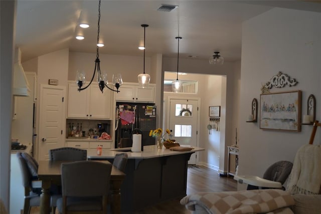 kitchen featuring white cabinets, black fridge, vaulted ceiling, decorative light fixtures, and dark hardwood / wood-style flooring