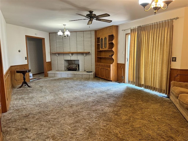 carpeted living room featuring ceiling fan with notable chandelier, wood walls, and a fireplace