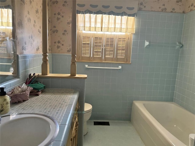 bathroom featuring a tub to relax in, vanity, tile walls, tile patterned flooring, and toilet