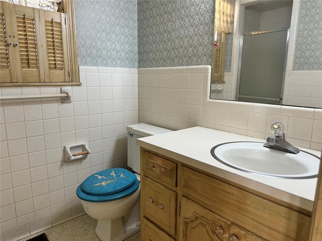 bathroom featuring a shower with door, vanity, tile walls, and toilet