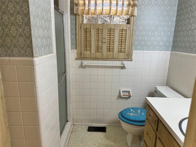 bathroom featuring tile patterned floors, walk in shower, vanity, tile walls, and toilet