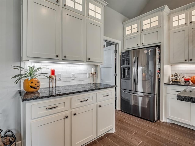 kitchen featuring stainless steel refrigerator with ice dispenser, dark hardwood / wood-style floors, dark stone countertops, tasteful backsplash, and white cabinetry