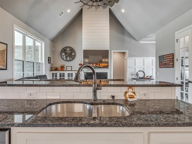 kitchen featuring sink, white cabinets, dark stone counters, and high vaulted ceiling