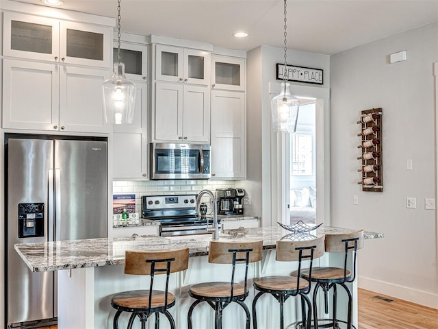 kitchen featuring white cabinets, appliances with stainless steel finishes, a center island with sink, and light stone counters