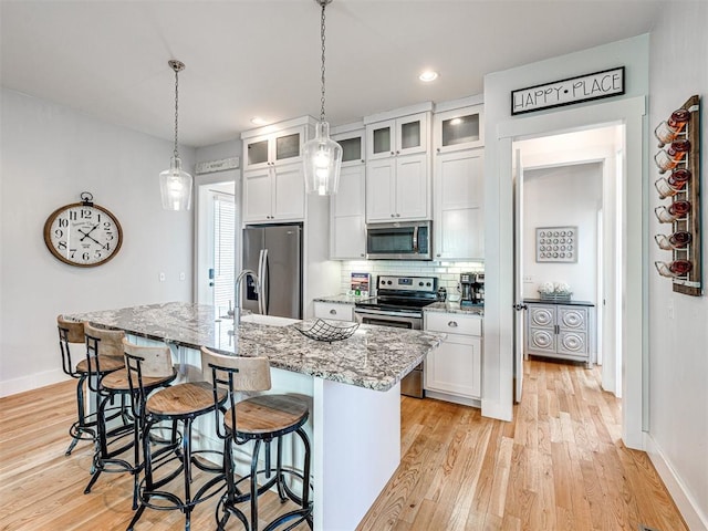 kitchen with a center island with sink, light hardwood / wood-style floors, light stone counters, white cabinetry, and stainless steel appliances