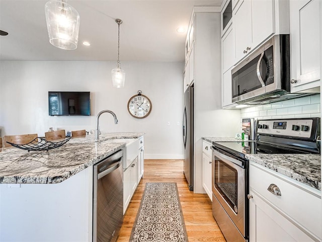 kitchen with light stone counters, light hardwood / wood-style flooring, pendant lighting, white cabinets, and appliances with stainless steel finishes