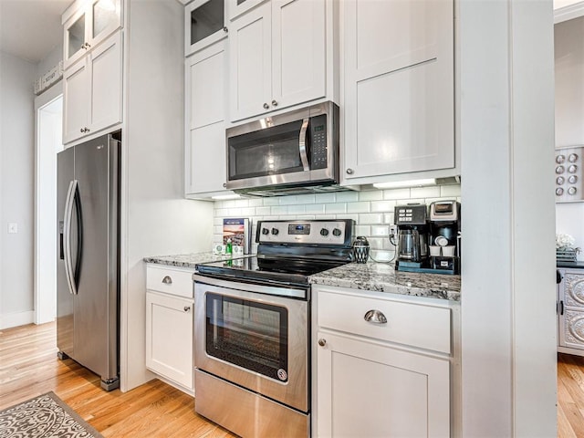 kitchen featuring light stone countertops, light wood-type flooring, tasteful backsplash, stainless steel appliances, and white cabinetry