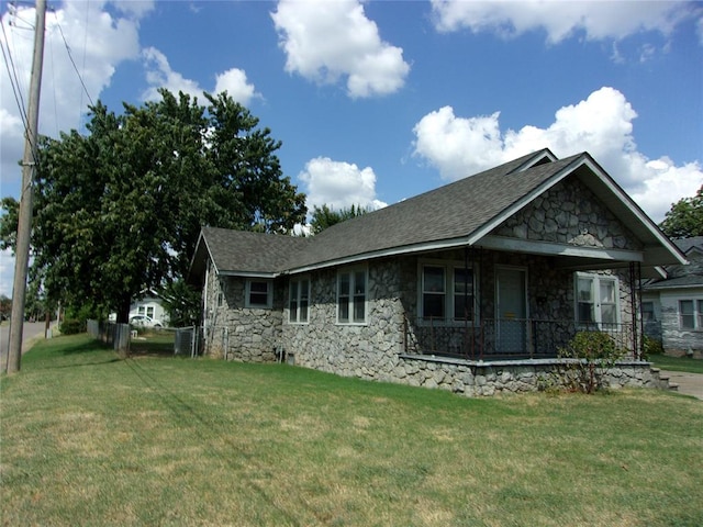 view of home's exterior featuring a porch, a lawn, stone siding, and a shingled roof