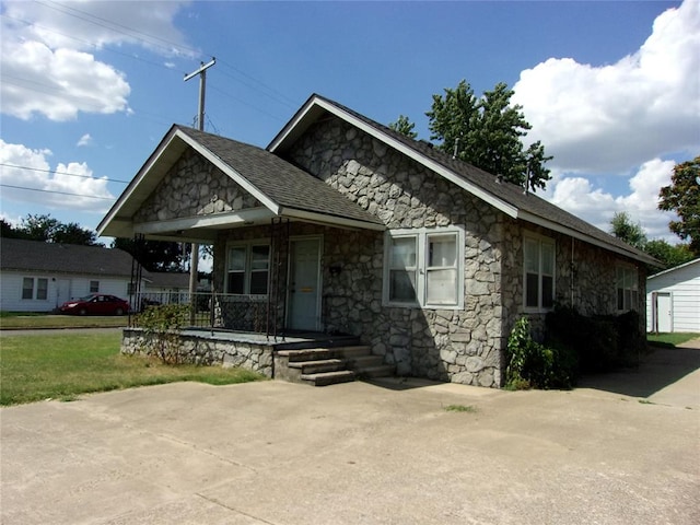 view of front of home with stone siding, a porch, an outdoor structure, and roof with shingles