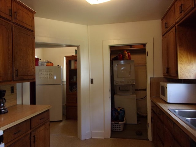 kitchen with light countertops, brown cabinetry, white appliances, stacked washer / drying machine, and a sink