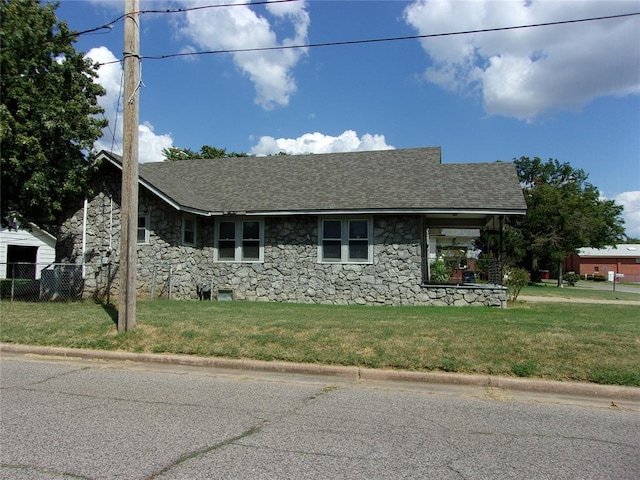 view of front facade with a front yard, fence, stone siding, and a shingled roof