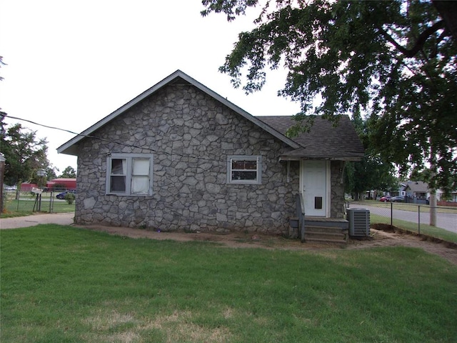 rear view of house with central air condition unit, roof with shingles, a yard, and fence