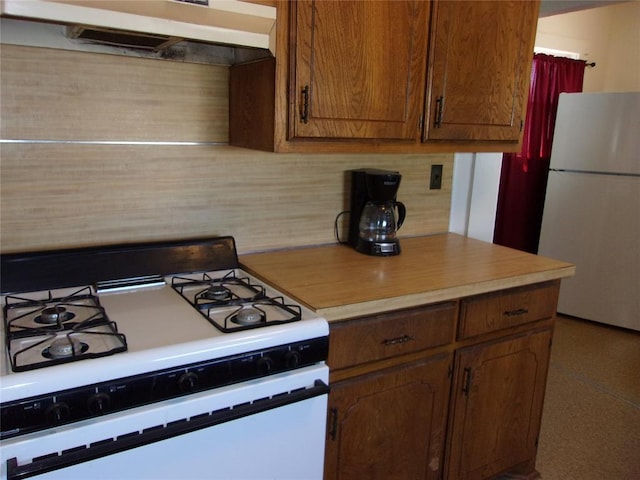 kitchen featuring white appliances, brown cabinetry, light countertops, under cabinet range hood, and backsplash