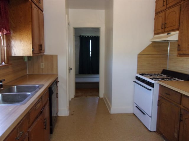 kitchen with white gas stove, under cabinet range hood, decorative backsplash, brown cabinetry, and a sink