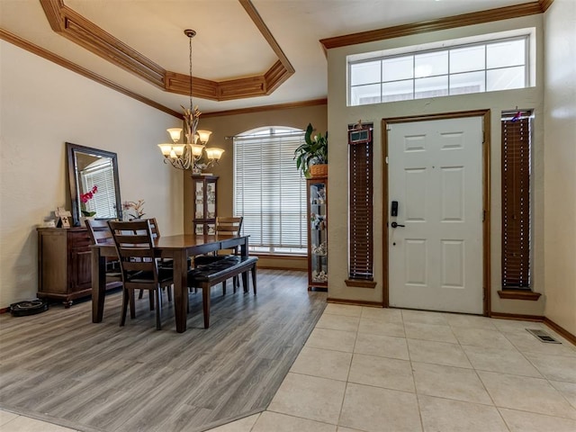 entryway featuring light hardwood / wood-style floors, a raised ceiling, crown molding, and a chandelier