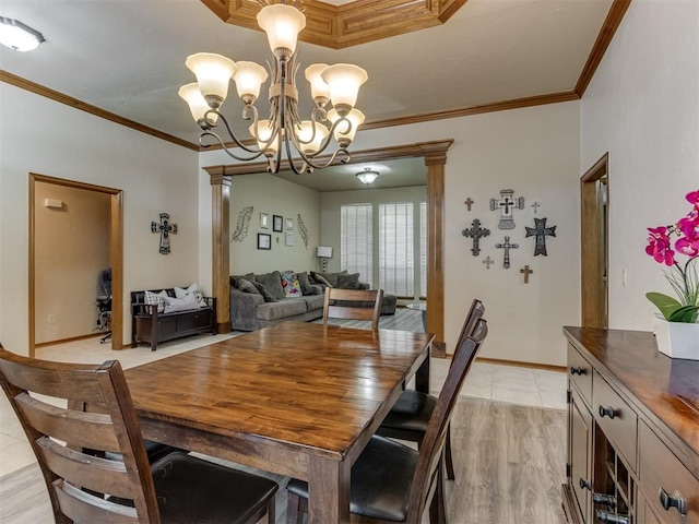 dining room featuring light wood-type flooring, an inviting chandelier, crown molding, and ornate columns