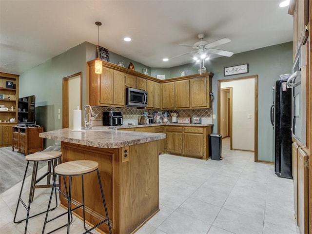 kitchen featuring black fridge, sink, ceiling fan, tasteful backsplash, and a kitchen bar