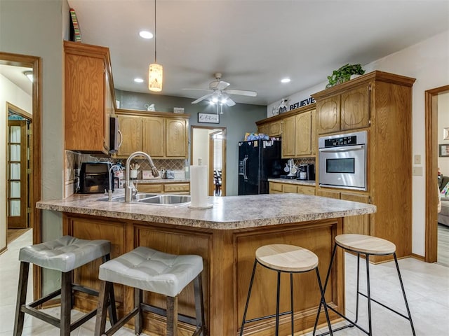 kitchen with decorative backsplash, appliances with stainless steel finishes, a breakfast bar, ceiling fan, and sink