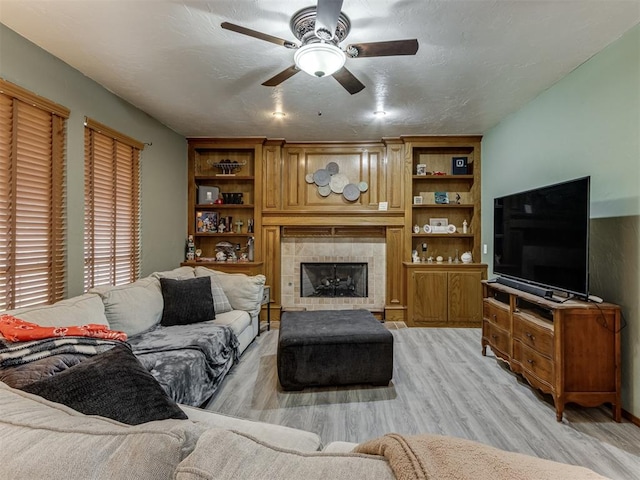 living room featuring ceiling fan, light wood-type flooring, a textured ceiling, and a tile fireplace