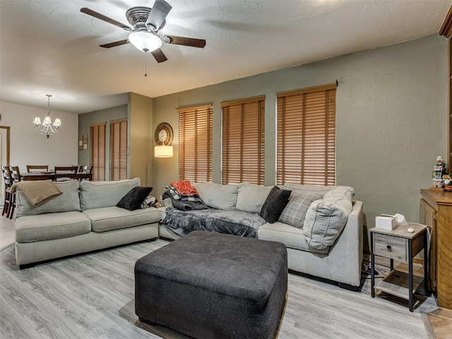 living room with ceiling fan with notable chandelier and light hardwood / wood-style flooring