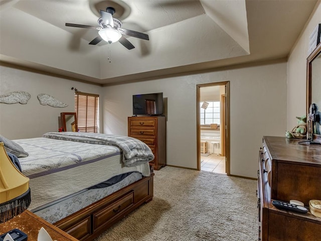 carpeted bedroom featuring ensuite bathroom, ceiling fan, and a tray ceiling