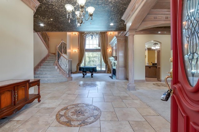 foyer featuring stairway, crown molding, ornate columns, and a chandelier