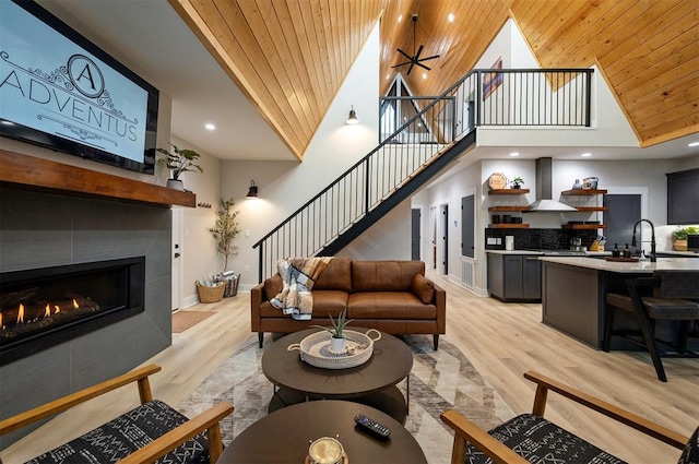 living room with a tiled fireplace, high vaulted ceiling, wood ceiling, and light hardwood / wood-style floors