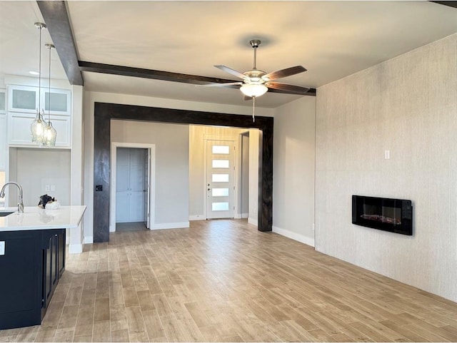 unfurnished living room with light hardwood / wood-style floors, sink, beam ceiling, and ceiling fan