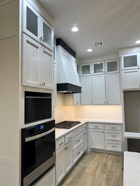 kitchen with white cabinetry, wall oven, custom range hood, and stainless steel gas cooktop