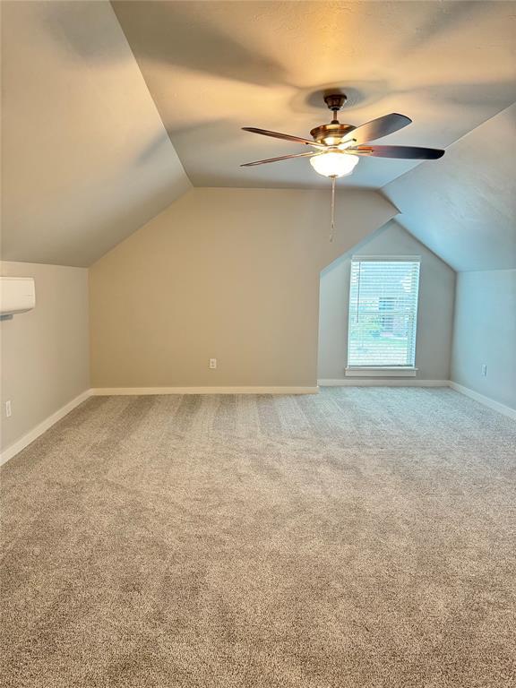 additional living space with vaulted ceiling, carpet, ceiling fan, and a wall unit AC