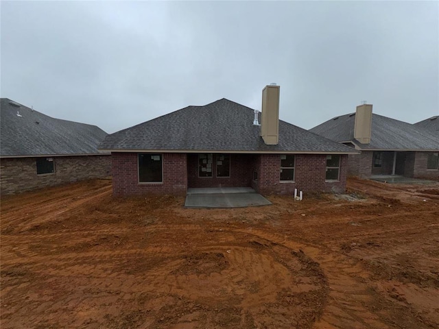 back of house with brick siding, roof with shingles, and a patio area