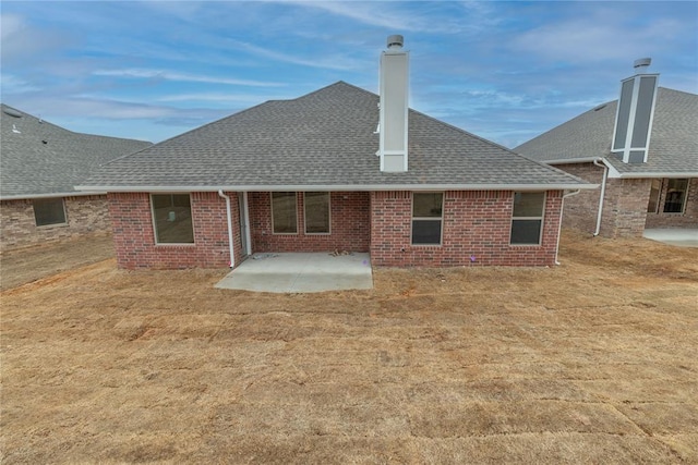 back of property with a shingled roof, a chimney, a patio area, and brick siding