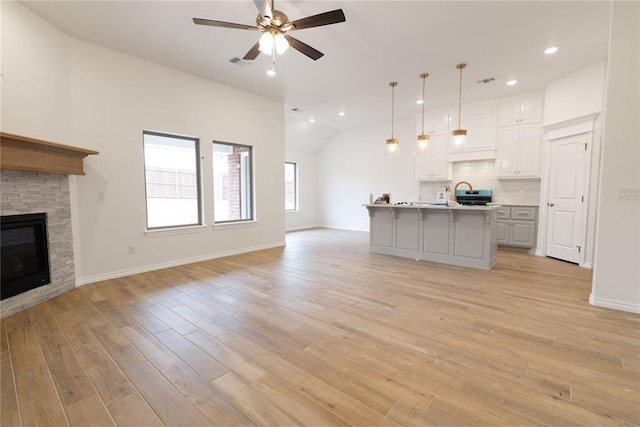 unfurnished living room with a fireplace, a sink, visible vents, a ceiling fan, and light wood-style floors