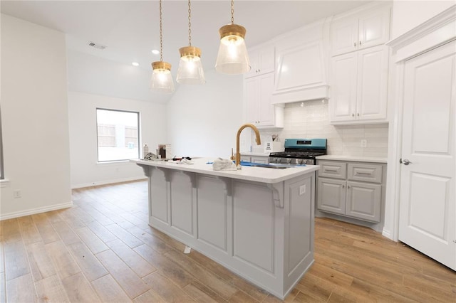 kitchen featuring stainless steel gas stove, decorative backsplash, light countertops, premium range hood, and a sink