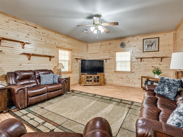 living room with wood walls, ceiling fan, a healthy amount of sunlight, and light wood-type flooring