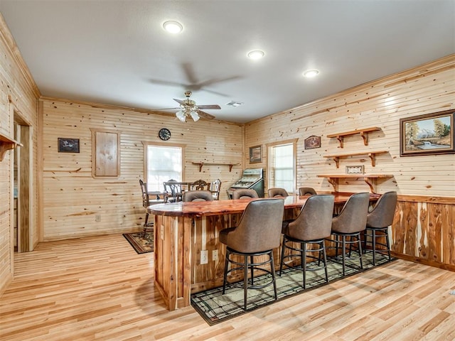 kitchen with wood walls, ceiling fan, light wood-type flooring, a kitchen bar, and kitchen peninsula