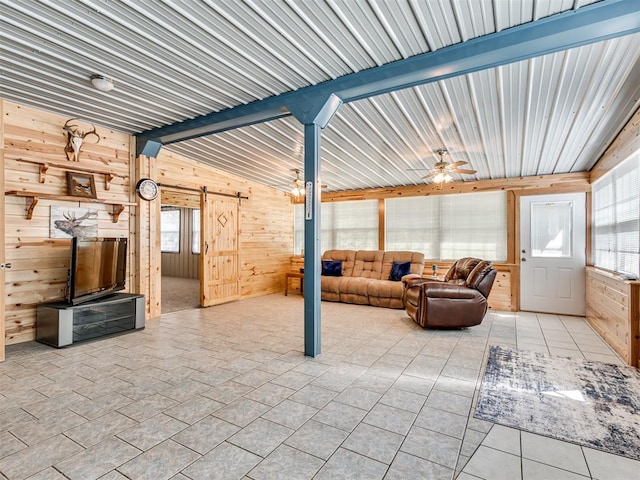 living room with a barn door, wooden walls, a wealth of natural light, and vaulted ceiling with beams