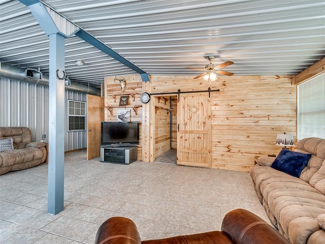 living room with ceiling fan, a barn door, lofted ceiling, and wooden walls