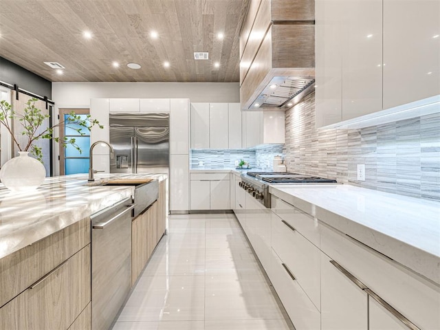 kitchen with light tile patterned floors, a barn door, premium range hood, white cabinets, and appliances with stainless steel finishes