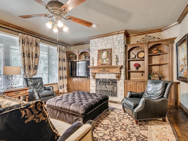 living room with ceiling fan, dark wood-type flooring, a stone fireplace, a textured ceiling, and ornamental molding