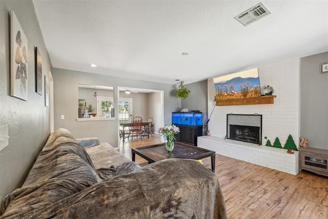 living room with a fireplace, ceiling fan, and light hardwood / wood-style flooring