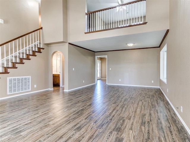 unfurnished living room with a towering ceiling, wood-type flooring, and ornamental molding