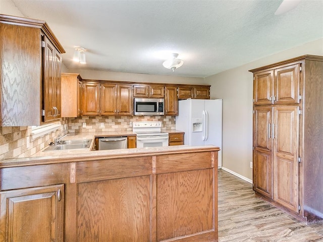 kitchen with sink, tasteful backsplash, light hardwood / wood-style floors, kitchen peninsula, and stainless steel appliances