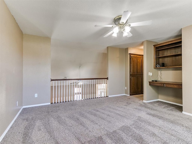 unfurnished room featuring ceiling fan, built in desk, and light colored carpet