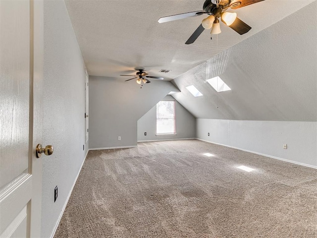 bonus room featuring vaulted ceiling with skylight, ceiling fan, carpet floors, and a textured ceiling