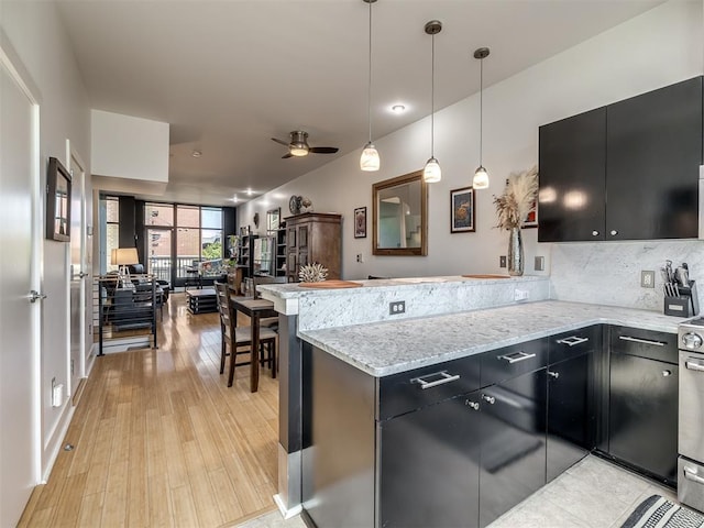 kitchen with kitchen peninsula, light stone countertops, ceiling fan, pendant lighting, and light hardwood / wood-style flooring