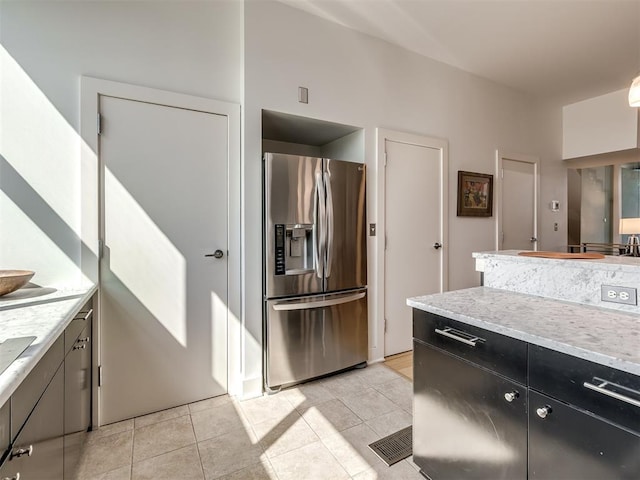 kitchen featuring stainless steel fridge with ice dispenser, light tile patterned floors, and light stone countertops