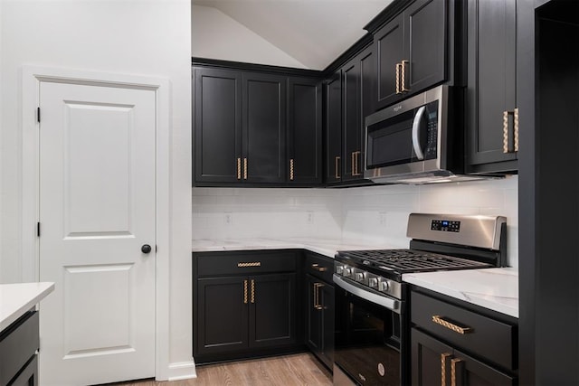 kitchen featuring stainless steel appliances, tasteful backsplash, light stone counters, vaulted ceiling, and light wood-type flooring