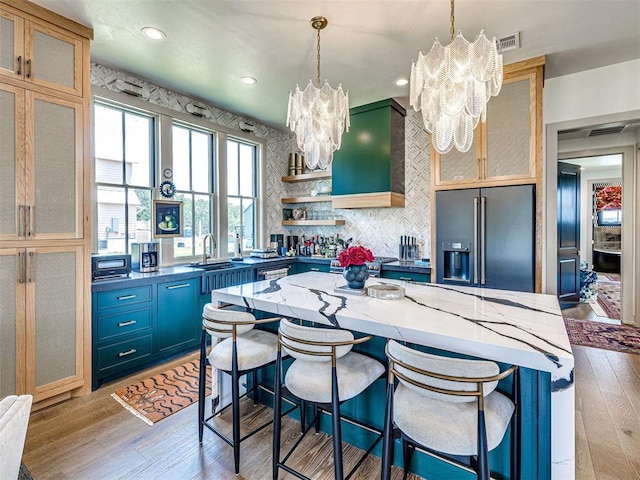 kitchen featuring blue cabinetry, dark stone countertops, built in refrigerator, and light wood-type flooring